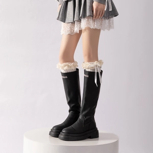 Close-up of black leather leg warmers with cream lace trim and white ribbon bow details