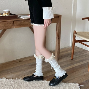 Detail of white knitted leg warmers with delicate lace trim and ribbon bow on top