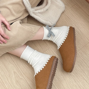 Close-up of brown suede slippers with white scalloped trim and a decorative grey bow