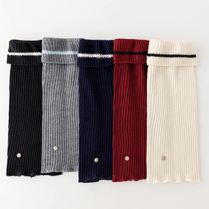Flat lay of knit leg warmers in five colors featuring striped tops and metal buckles