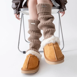 Detail of brown chunky knit leg warmers with metal logo paired with plush slippers