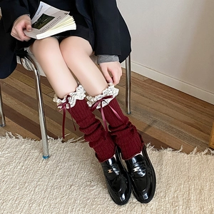 Close-up of wine red ribbed knit leg warmers with white lace trim and ribbon bows