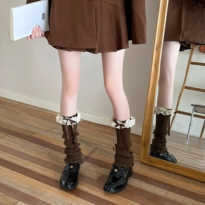 Close-up of dark brown knitted leg warmer featuring delicate white lace trim and bow detail