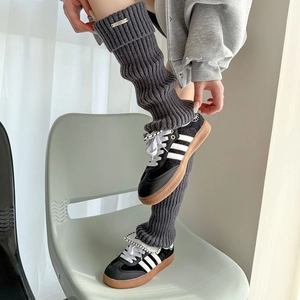 Detail of dark grey ribbed knit leg warmers with metallic logo tag in Y2K style