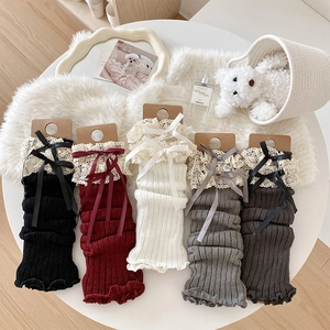 Detail of five colored knit leg warmers with lace trim and bows on a white table