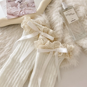 Detail of white knitted leg warmers with delicate lace trim and silk ribbons