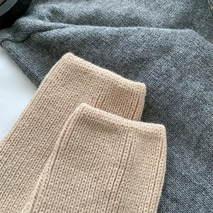 Macro shot of knitted leg warmers showing beige and grey ribbed wool texture details