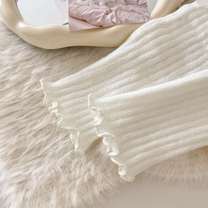 Detailed close-up of white knitted leg warmers with delicate lace trim and ribbed texture
