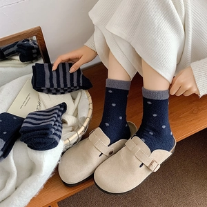 Detail of navy blue striped plush socks paired with beige suede mule shoes on a bench