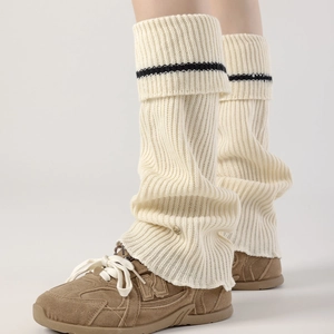 Detail of ribbed knit leg warmers in cream with black stripe and metal charm accents