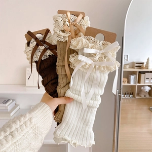 Close-up of knit leg warmers with delicate lace trim and ribbon bows in three colors