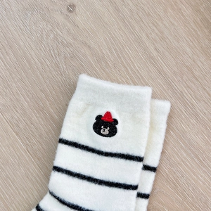 Close-up of white plush thermal socks with black stripes and cute bear embroidery