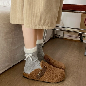 Detail of grey polka dot socks with white fur trim and bows paired with brown mules