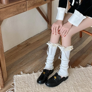 Close-up of white knitted leg warmers featuring delicate lace trim and satin bows