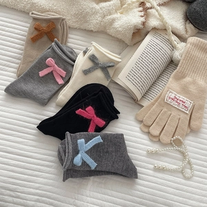Flat lay of knit crew socks with bow details and matching gloves on white bedding