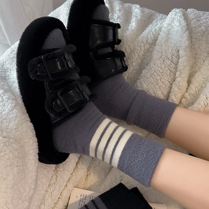 Close-up of black fuzzy slippers with leather straps over gray striped warm cotton socks