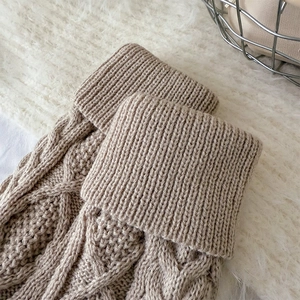 Gros plan de jambières en grosse maille torsadée sur un tapis moelleux blanc