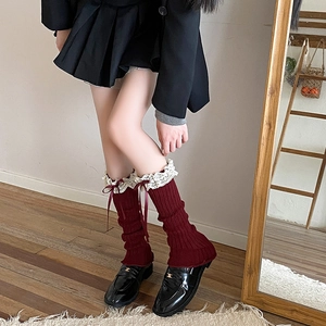 Detail view of burgundy knitted leg warmers with delicate white lace trim and satin bows