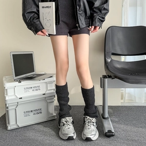Close-up of dark grey ribbed knit leg warmers styled with silver sneakers and black leather