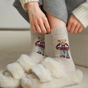 Detail of knitted beige wool socks with cute festive brown bear pattern and rib cuff
