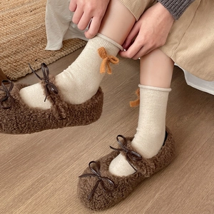 Close-up of cream knit mid-calf socks with orange bows and brown fuzzy Mary Jane shoes