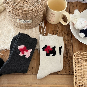 Detail view of thick wool socks featuring 3D plush puppy and red bow on wooden background