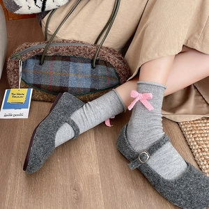 Detail of grey Mary Jane wool shoes with knit socks featuring pink bows and metal buckles