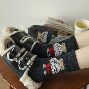 Close-up of cozy wool socks with bear embroidery paired with plush leather slippers