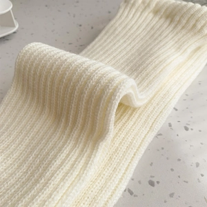 Close-up of thick white ribbed knit leg warmers showing texture on stone background