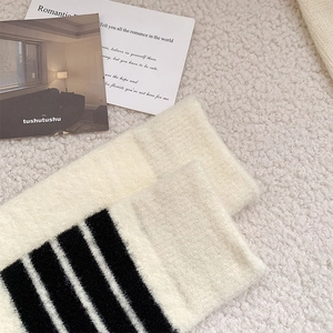 Detail of warm knit striped mid-calf socks on a cozy white sheepskin texture background
