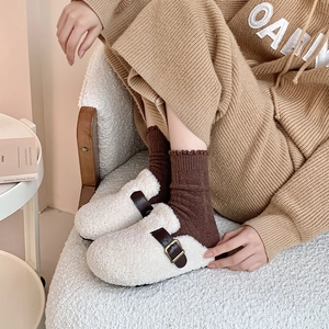Detail of cream plush mule shoes with brown leather strap and warm knit socks in home setting