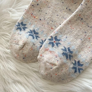 Makroaufnahme dicker Wollsocken mit blauen Schneeflocken und bunten Strickpunkten