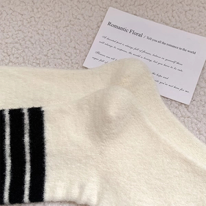 Close-up of thick cream knit socks with black stripes on soft plush background