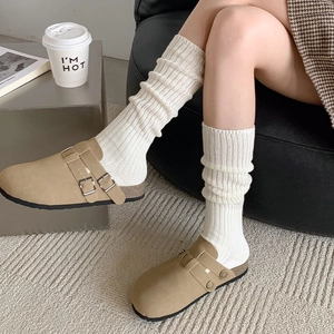 Close-up of sand suede clogs paired with white ribbed knit socks in a home setting
