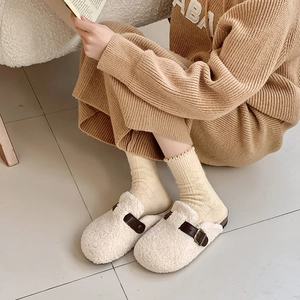 Close-up of cream winter slippers with fleece texture and brown leather strap buckle