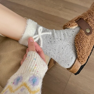 Detail of grey tweed knit socks with white faux fur trim and a delicate bow tie