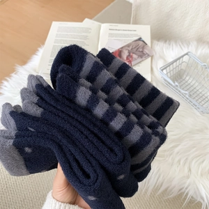 Close-up of thick knit striped winter socks in navy blue and grey on a plush mat