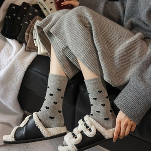 Close-up of grey wool socks featuring black heart patterns and ribbed cuffs for winter
