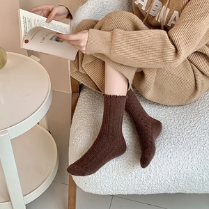 Detail of dark brown knit socks with ruffled edges and cable pattern in home setting