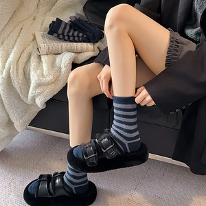 Detail of navy striped plush socks paired with black fur slippers on a white soft blanket