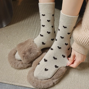 Close-up of beige knitted socks with black heart patterns and ribbed cuffs for winter