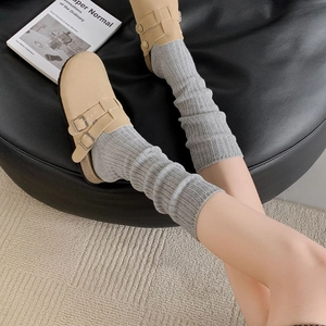 Detail of beige buckle mules paired with grey ribbed knit slouch socks on a plush rug