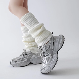 Detailed close-up of cream white vertical ribbed knit leg warmers worn with sneakers