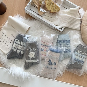 Wollsocken mit Schneeflockenmuster in Reißverschlussbeuteln auf weißem Plüschteppich