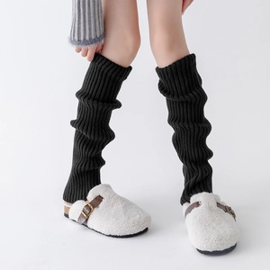 Detailed view of black vertical ribbed knit leg warmers paired with white fuzzy slippers