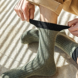 Detailed texture of men's thick wool crew socks in army green with black ribbed cuffs