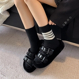 Detail of plush black double-strap faux fur slippers worn with striped warm socks