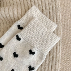 Close-up of white knitted socks featuring black heart jacquard and ribbed cuff texture