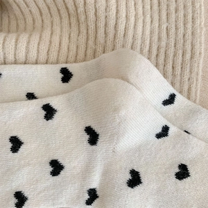 Close-up of white knit socks with black heart patterns showing soft wool texture