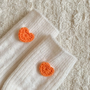 Vue détaillée de chaussettes en laine blanche avec patchs en forme de cœur orange
